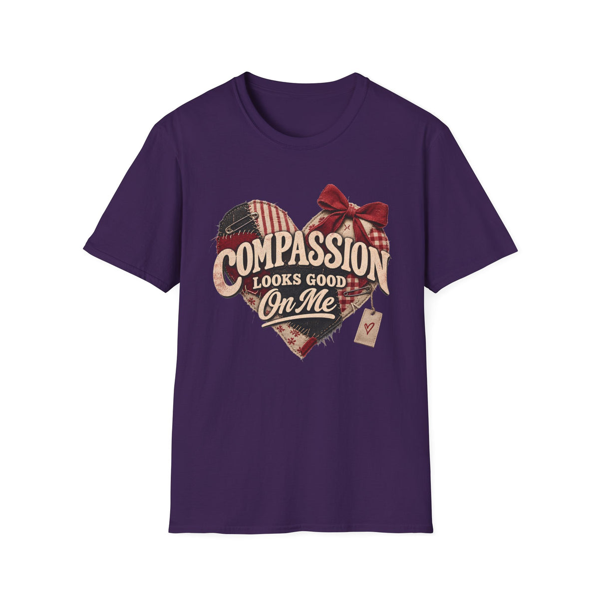 A purple short-sleeve crewneck t-shirt with a graphic on the front. The graphic features a heart made of plaid and flag patterns, a red bow, and the text 'COMPASSION LOOKS GOOD On Me' in a vintage style.