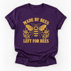 A purple short-sleeve crewneck t-shirt with a yellow graphic of a bee, honeycomb, and flowers, with the text 'MADE BY BEES LEFT FOR BEES' printed on the front, shown against a plain white background.