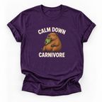 A purple short-sleeve crewneck t-shirt featuring a cartoon capybara eating green leaves with the text 'CALM DOWN CARNIVORE' printed in white above and below the graphic.