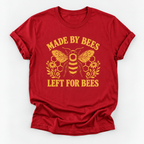 A red short-sleeve crewneck t-shirt with a yellow graphic print featuring a bee, honeycomb, flowers, and the text 'MADE BY BEES LEFT FOR BEES' on a light gray background.