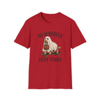 A red short-sleeve crewneck t-shirt featuring a Halloween graphic of a ghost riding a skateboard with a jack-o'-lantern, with the text 'NO SCHEDULE JUST VIBES' printed in black.