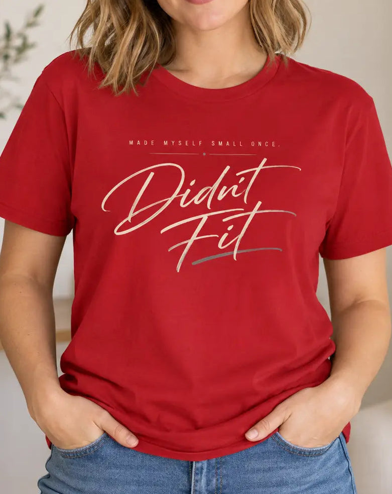 A woman wearing a red graphic t-shirt with the text 'Didnt Fit' in white and gray script, standing in a brightly lit, modern living room.
