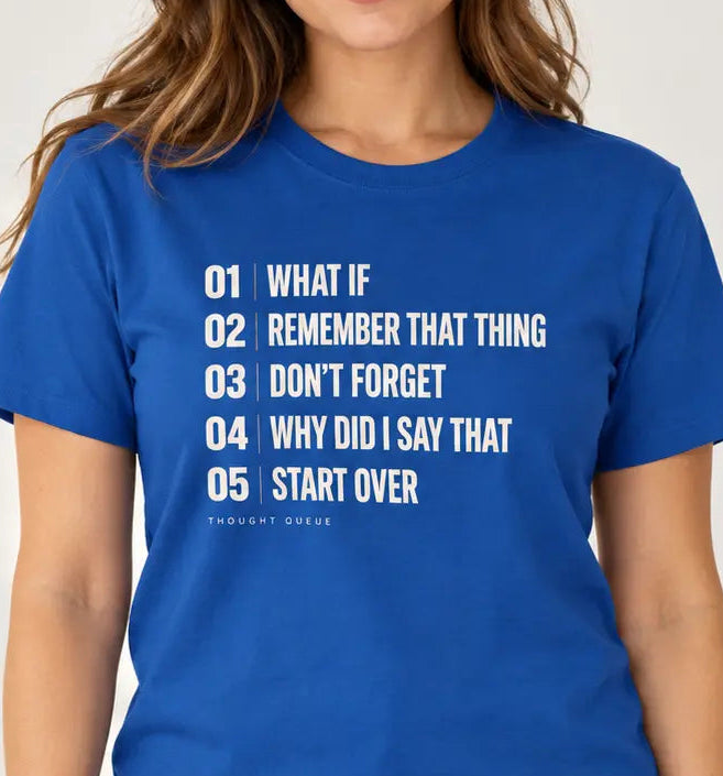 Woman wearing royal blue graphic T-shirts featuring a cream numbered “Thought Queue” list with the phrases “What If,” “Remember That Thing,” “Don’t Forget,” “Why Did I Say That,” and “Start Over.”