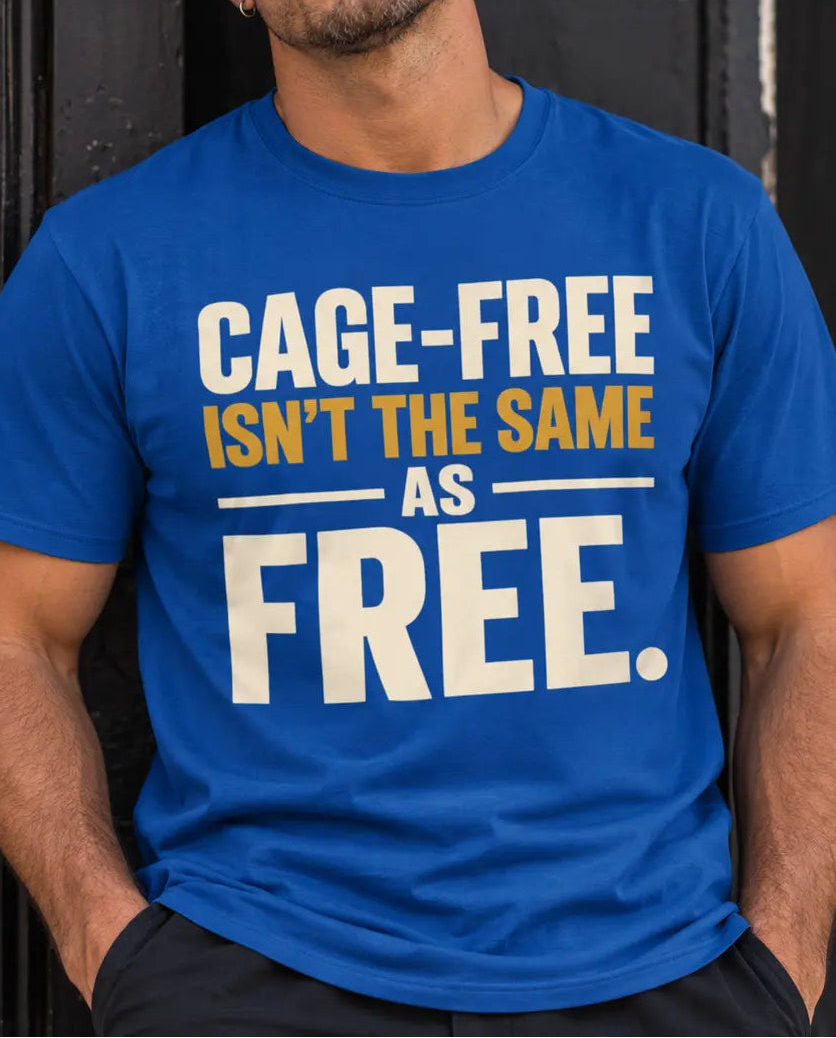 A man wearing a bright blue graphic t-shirt with the text 'CAGE-FREE ISN'T THE SAME AS FREE.' printed in white and yellow, leaning against a dark wooden door.