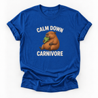 A royal blue short-sleeve t-shirt with a graphic of a capybara eating green leaves, surrounded by the text 'CALM DOWN CARNIVORE' in white. The t-shirt is displayed flat against a clean white background.