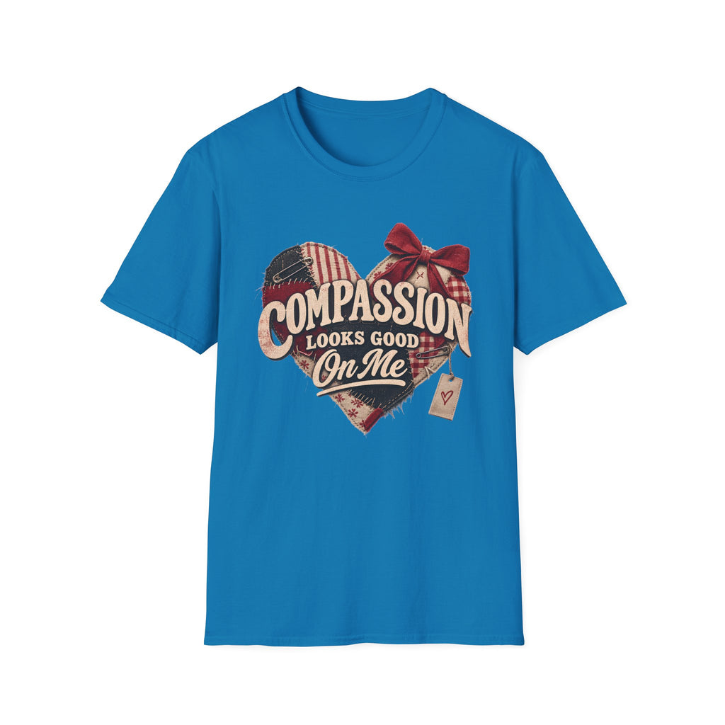 A bright blue short-sleeve crewneck t-shirt with a graphic on the chest. The graphic features a distressed heart made of red, white, and blue plaid patterns, adorned with a red bow, and the text 'COMPASSION LOOKS GOOD On Me' in a vintage font, with a small price tag hanging from the bow.