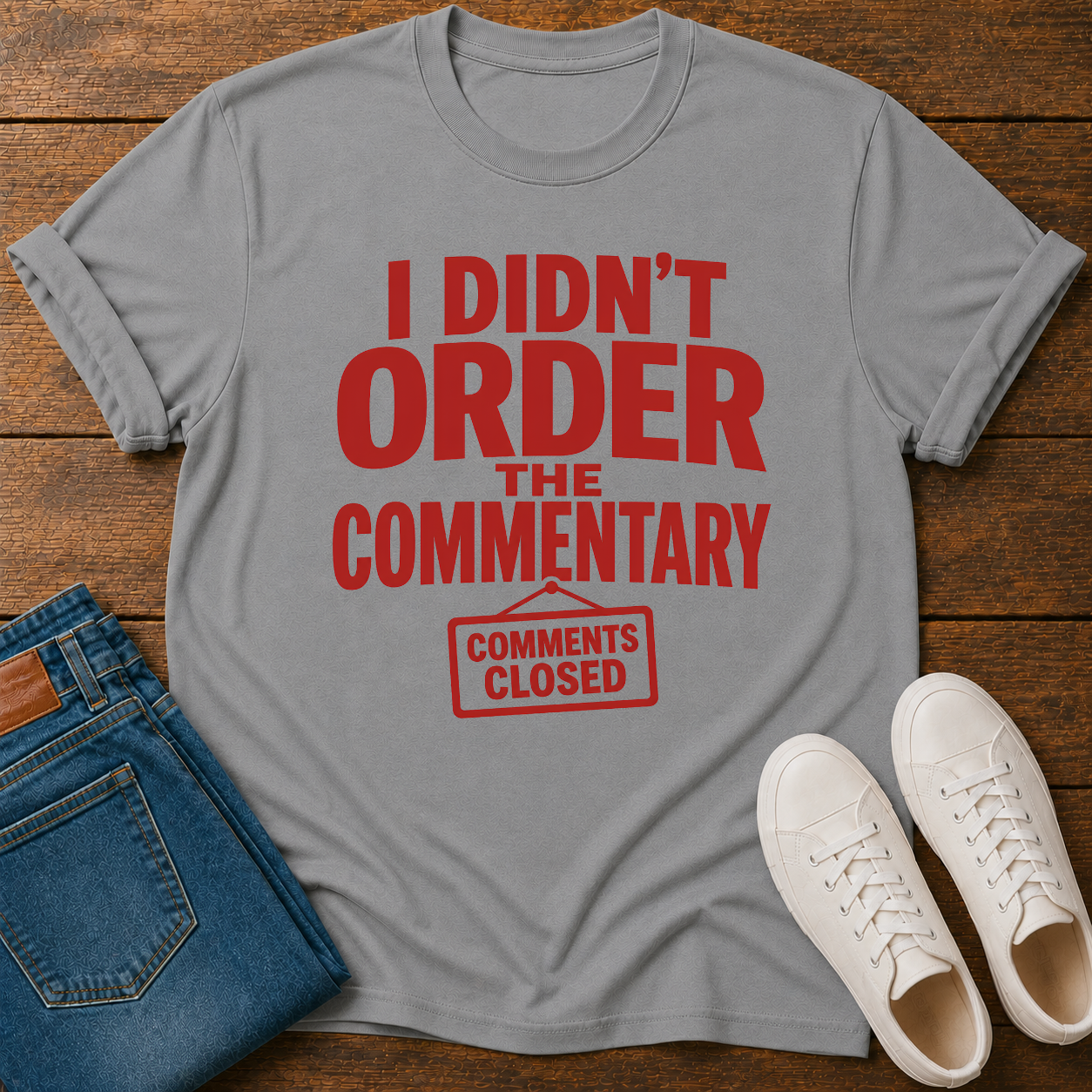 Gray t-shirt with red text 'I Didn't Order the Commentary' on a wooden surface with jeans and sneakers.