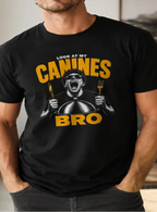 A man wearing a black graphic t-shirt with a humorous design that reads 'LOOK AT MY CANINES BRO' in yellow and white, standing in a modern indoor setting.
