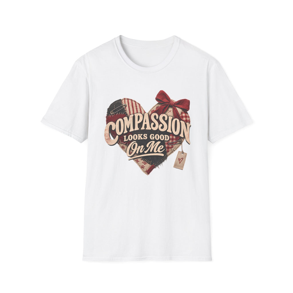 A white short-sleeve crewneck t-shirt featuring a rustic heart-shaped graphic with a red bow, plaid pattern, and the text 'COMPASSION LOOKS GOOD ON ME' in a vintage font.