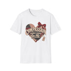 A white short-sleeve crewneck t-shirt featuring a rustic heart-shaped graphic with a red bow, plaid pattern, and the text 'COMPASSION LOOKS GOOD ON ME' in a vintage font.