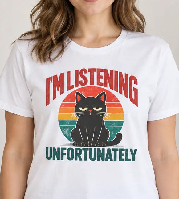 A woman wearing a white graphic t-shirt with a retro-style design that reads 'I'M LISTENING UNFORTUNATELY' around a black cat silhouette on a sunset gradient. She is standing in a cozy, modern room with a wooden cabinet, framed art, and a wicker chair.