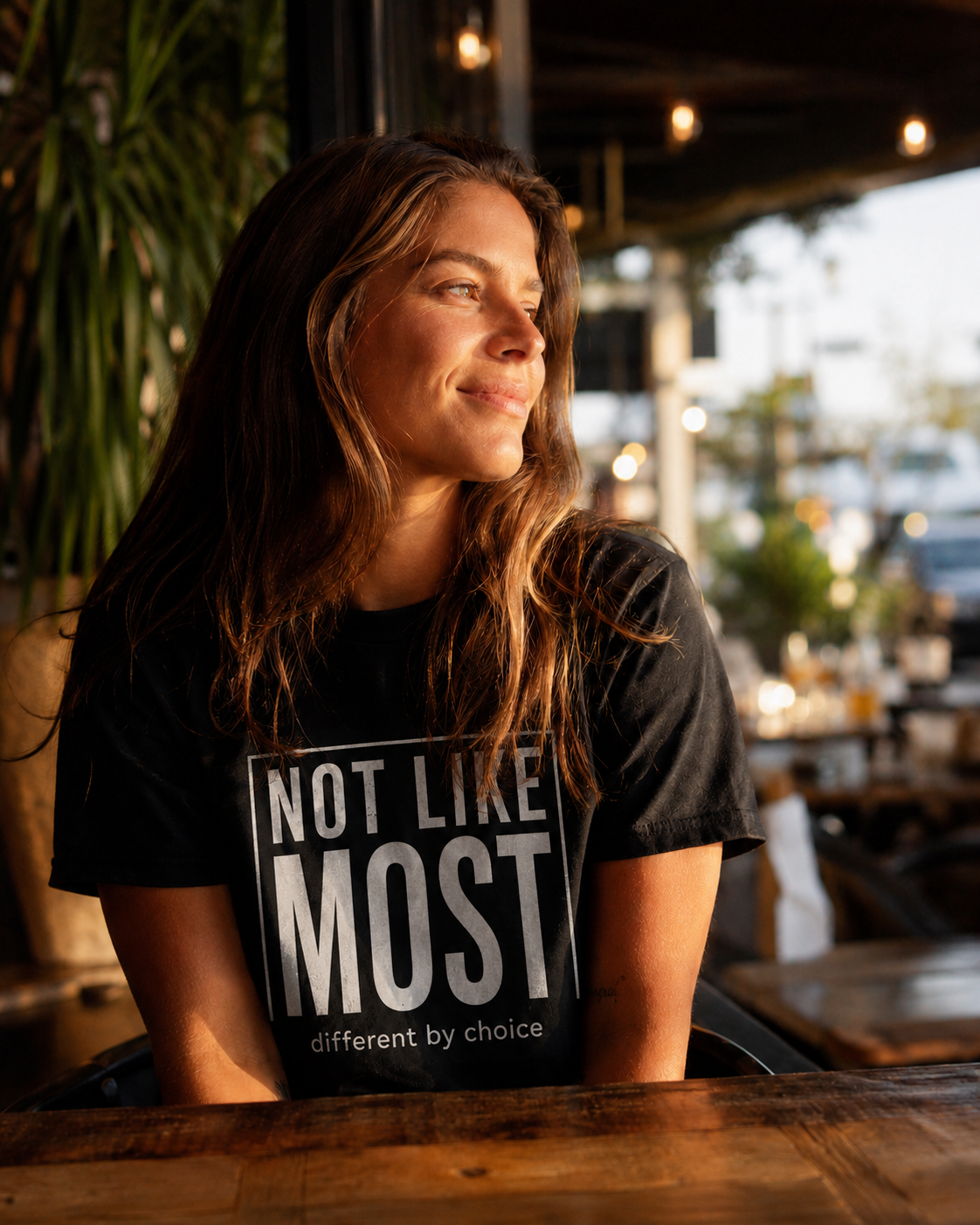 Woman wearing a black t-shirt with 'Not Like Most' text in a casual setting.