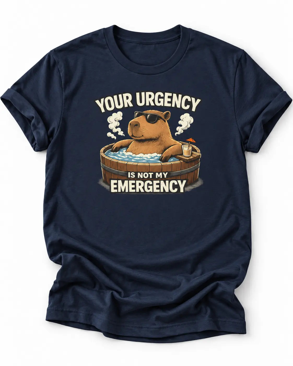 A navy blue short-sleeve crewneck t-shirt featuring a cartoon graphic of a capybara relaxing in a hot tub with the text 'YOUR URGENCY IS NOT MY EMERGENCY'.
