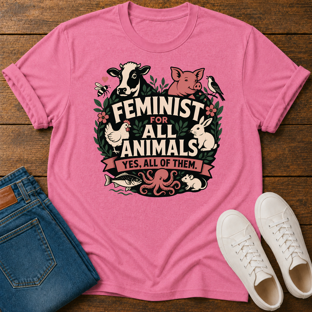 A pink graphic t-shirt laid flat on a wooden surface, styled with folded blue jeans and white sneakers. The t-shirt features a colorful graphic of various animals (cow, pig, chicken, rabbit, octopus, fish) surrounding the text 'FEMINIST FOR ALL ANIMALS YES, ALL OF THEM.