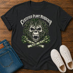 A black graphic t-shirt featuring a skull made of leaves and branches with the text 'CERTIFIED PLANT MURDERER' above it, styled in a flat lay on a wooden surface with blue jeans and white sneakers.