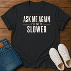 A black graphic t-shirt with the text 'ASK ME AGAIN I'LL SAY IT SLOWER' in white, styled in a flat lay on a wooden background with blue jeans and white sneakers.