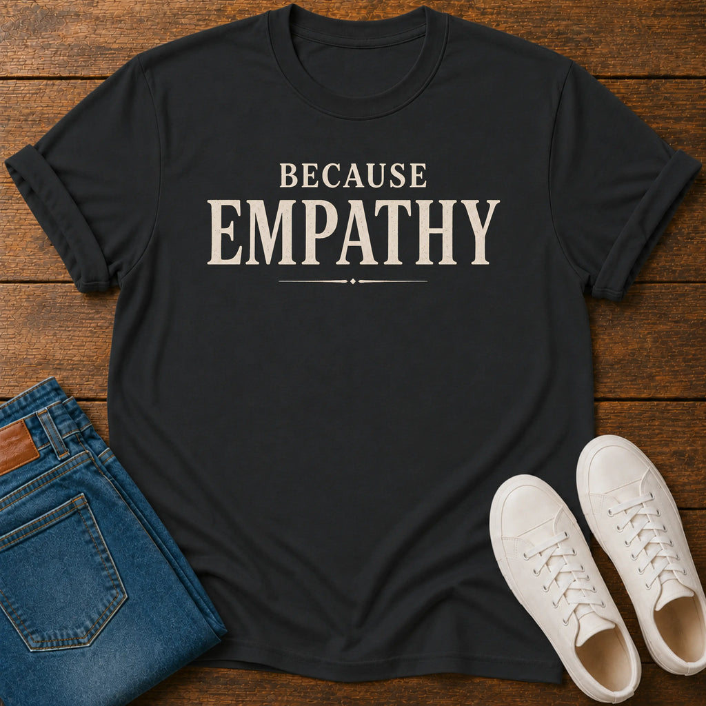 A black-shirt with the word 'EMPATHY' printed in large cream-colored letters, styled in a flat lay on a wooden background alongside folded blue jeans and a pair of white sneakers.