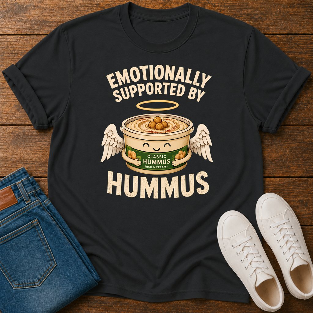 A black graphic t-shirt laid flat on a wooden surface, styled with folded blue jeans and white sneakers. The t-shirt features a cartoon graphic of a bowl of hummus with angel wings and the text 'EMOTIONALLY SUPPORTED BY HUMMUS'.