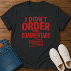 Black t-shirt with red text on a wooden surface with jeans and sneakers.