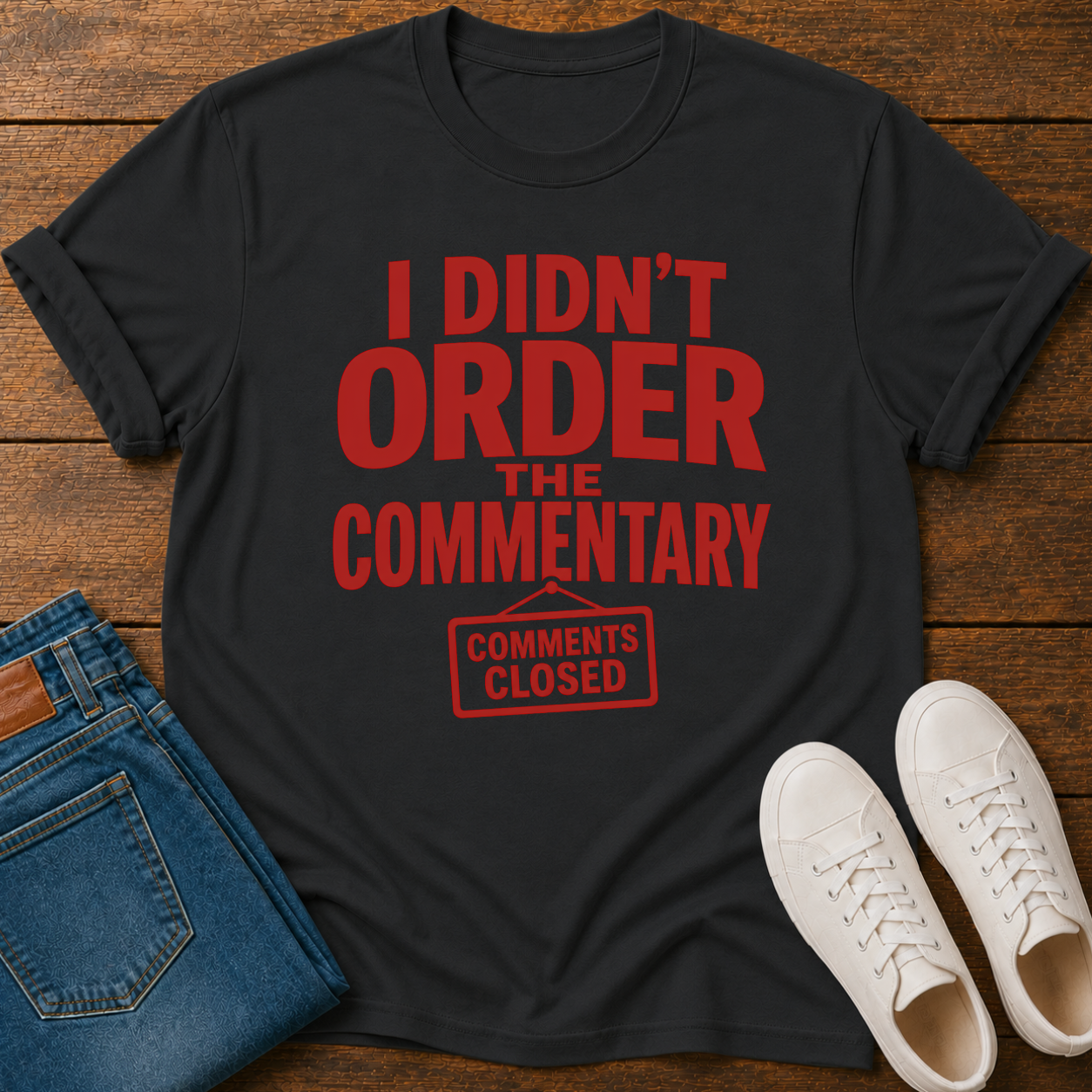 Black t-shirt with red text on a wooden surface with jeans and sneakers.