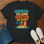 A black graphic t-shirt laid flat on a wooden surface, styled with blue jeans and white sneakers. The t-shirt features a colorful retro graphic with the text 'DESERTED ISLAND QUESTION AGAIN?' and cartoon characters on a small island.
