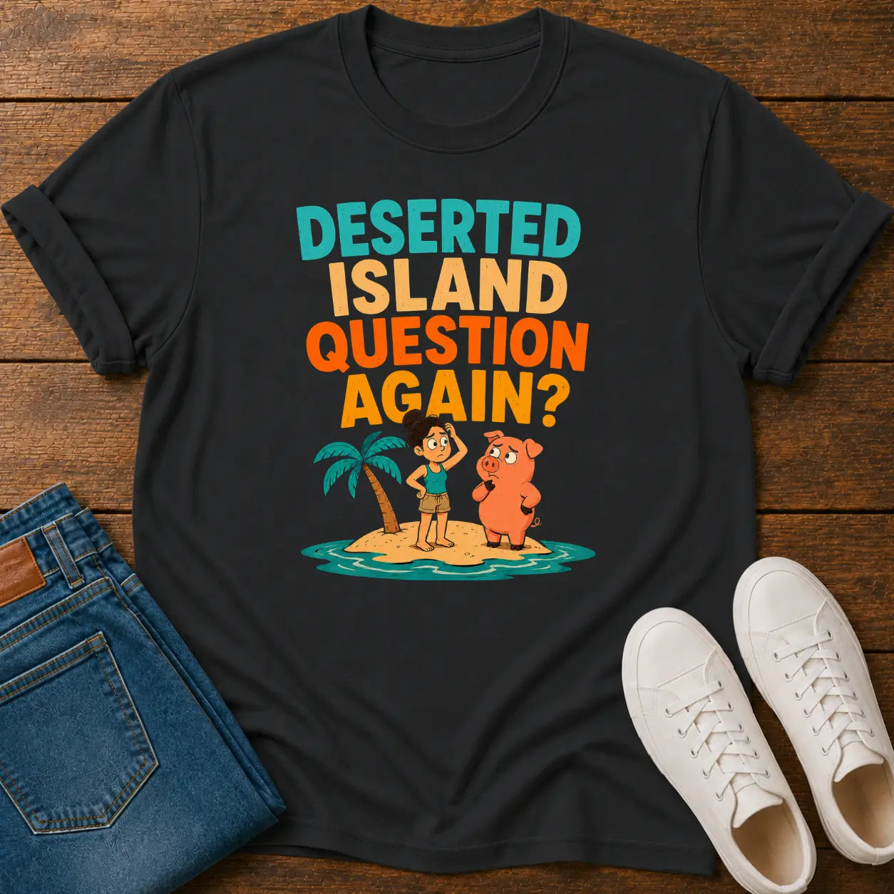 A black graphic t-shirt laid flat on a wooden surface, styled with blue jeans and white sneakers. The t-shirt features a colorful retro graphic with the text 'DESERTED ISLAND QUESTION AGAIN?' and cartoon characters on a small island.