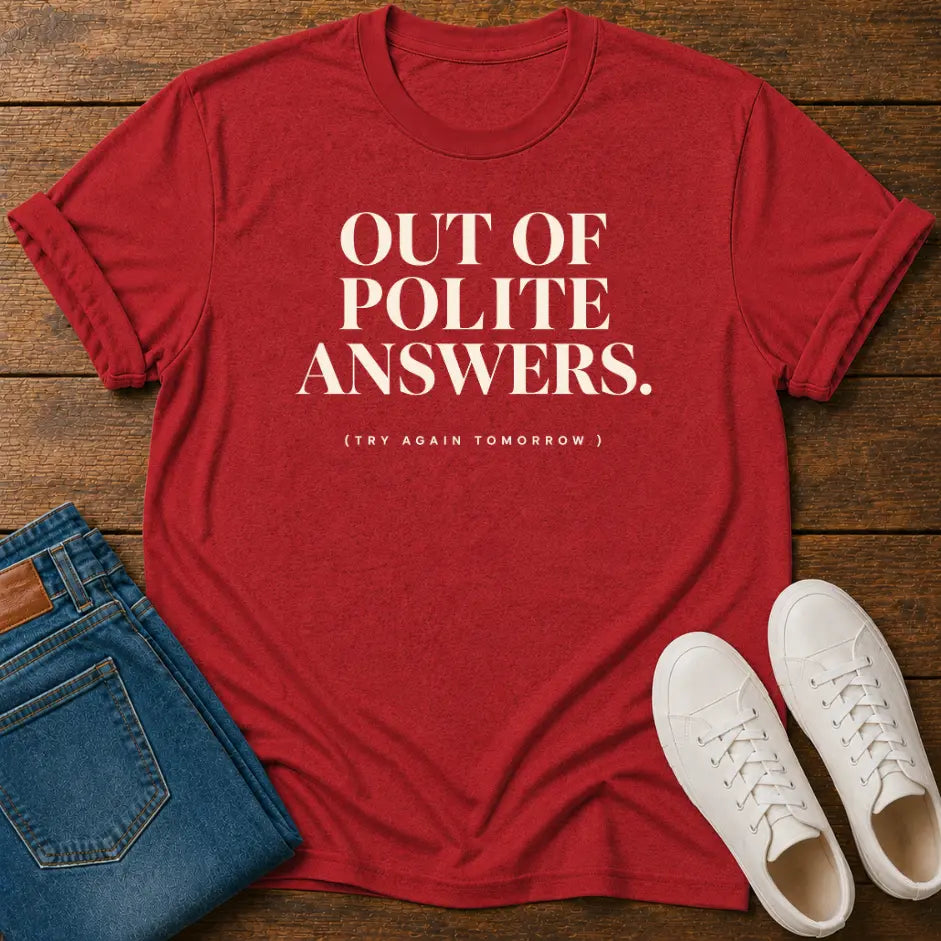 A red short-sleeve graphic T-shirt laid flat on a wooden surface, styled with folded blue jeans and a pair of white sneakers. The shirt has large white text reading “OUT OF POLITE ANSWERS.
