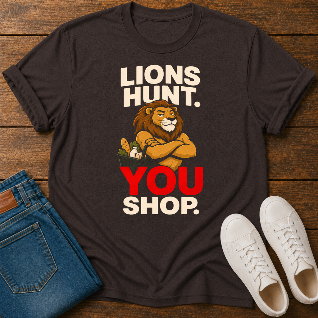 A dark brown graphic t-shirt laid flat on a wooden surface, styled with folded blue jeans and white sneakers. The t-shirt features a graphic of a lion with crossed arms holding a shopping cart, with the text 'LIONS HUNT.YOU SHOP'