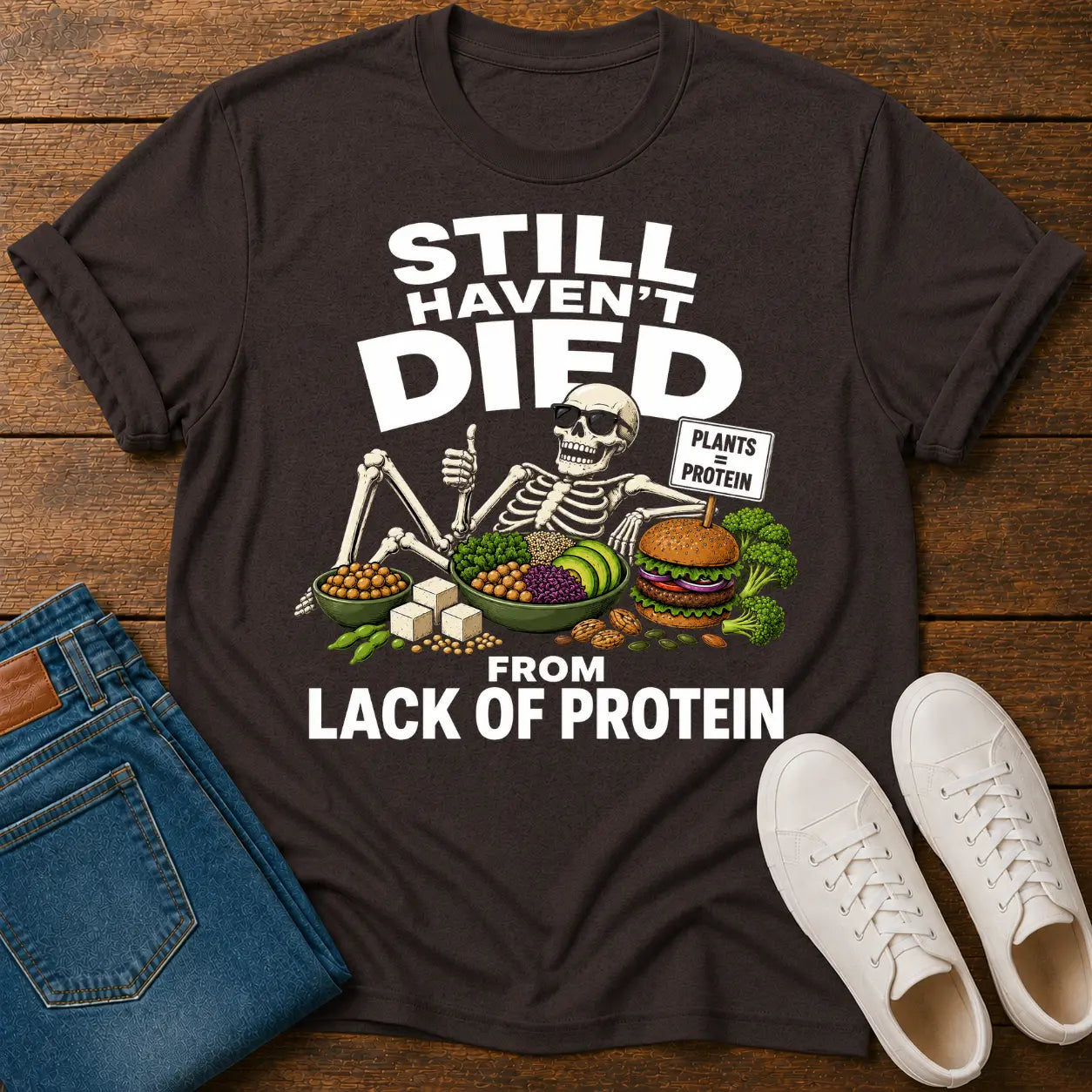 brown t=shirt with a skeleton graphic and text 'still haven't dies from lack of protein'