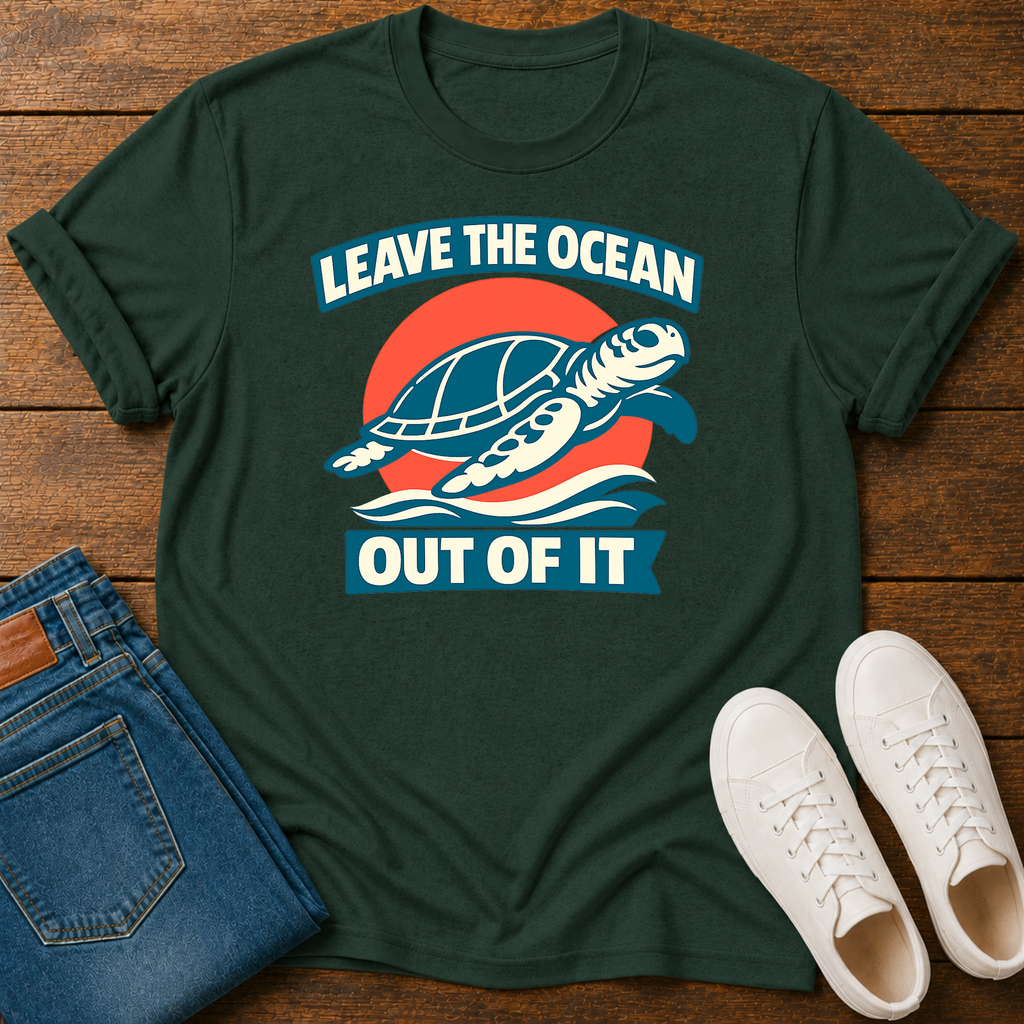 A dark green graphic t-shirt laid flat on a wooden surface, styled with folded blue jeans and white sneakers. The t-shirt features a graphic of a sea turtle swimming in front of a red and orange sun, with the text 'LEAVE THE OCEAN OUT OF IT' in white and blue.