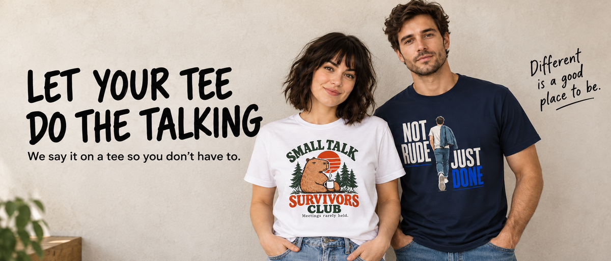 A man and a woman stand indoors wearing graphic T-shirts. The woman wears a white T-shirt with a bear and trees graphic reading 'Small Talk Survivors Club,' and the man wears a navy T-shirt with a blue and white graphic reading 'Not Rude Just Done.