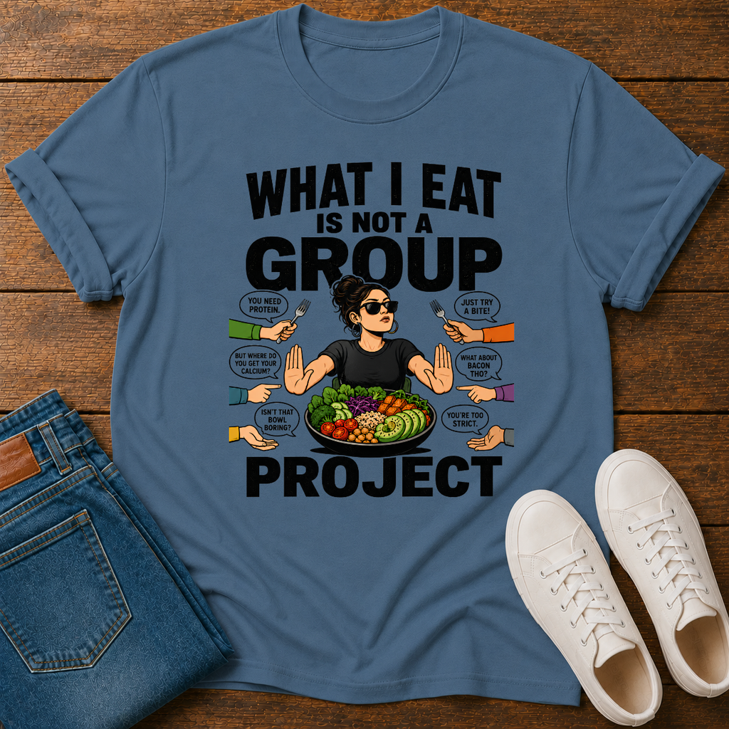 indigo blue t-shirt with a graphic of a woman eating salad and non vegan questions being thrown at her with text 'what i eat is not a group project" on a wooden board with jeans and sneakers