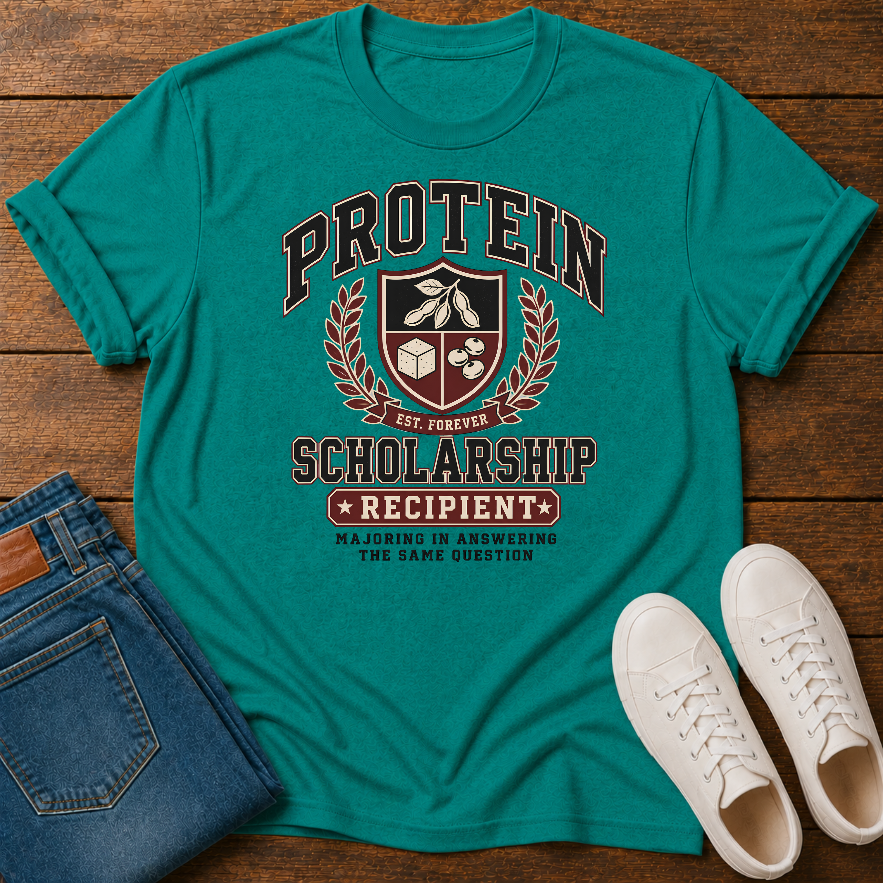 jade green t-shirt with Vintage collegiate crest design reading “Protein Scholarship Recipient” with soybean, tofu, and bean illustrations and the words “Majoring in Answering the Same Question.”