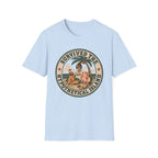 A light blue crewneck t-shirt featuring a circular retro-style graphic on the chest with awo man and a dog on a beach under a palm tree, with the text 'SURVIVED THE HYPOTHETICAL ISLAND'.