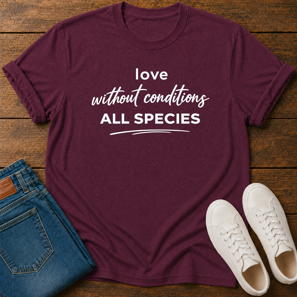 A maroon short-sleeve graphic T-shirt laid flat on a wooden surface, styled with folded blue jeans and a pair of white sneakers. The shirt has white text reading 'love without conditions ALL SPECIES'.