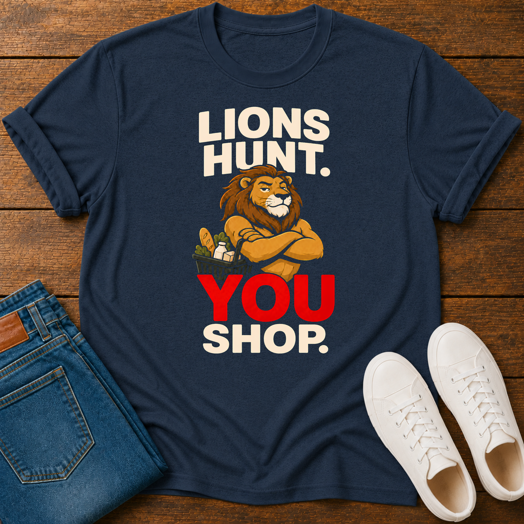A navy blue graphic t-shirt laid flat on a wooden surface, styled with folded blue jeans and white sneakers. The t-shirt features a cartoon lion with crossed arms and the text 'LIONS HUNT.