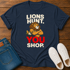 A navy blue graphic t-shirt laid flat on a wooden surface, styled with folded blue jeans and white sneakers. The t-shirt features a cartoon lion with crossed arms and the text 'LIONS HUNT.