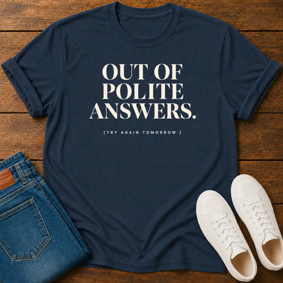A navy blue graphic t-shirt with the text 'OUT OF POLITE ANSWERS. (TRY AGAIN TOMORROW)' in white, styled in a flat lay on a wooden background with folded blue jeans and white sneakers.