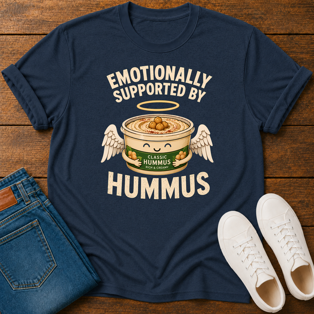 A navy blue graphic t-shirt laid flat on a wooden surface, styled with folded blue jeans and white sneakers. The t-shirt features a graphic of a cute angelic hummus bowl with wings, a halo, and the text 'EMOTIONALLY SUPPORTED BY HUMMUS' and 'CLASSIC HUMMUS GERMANY'.