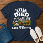 Navy blue t-shirt with skeleton graphic and text on a wooden surface with jeans and shoes.