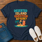 A navy blue graphic t-shirt laid flat on a wooden surface, styled with folded blue jeans and white sneakers. The t-shirt features a colorful cartoon graphic of a person and a dog on a small tropical island with the text 'DESERTED ISLAND QUESTION AGAIN?'.