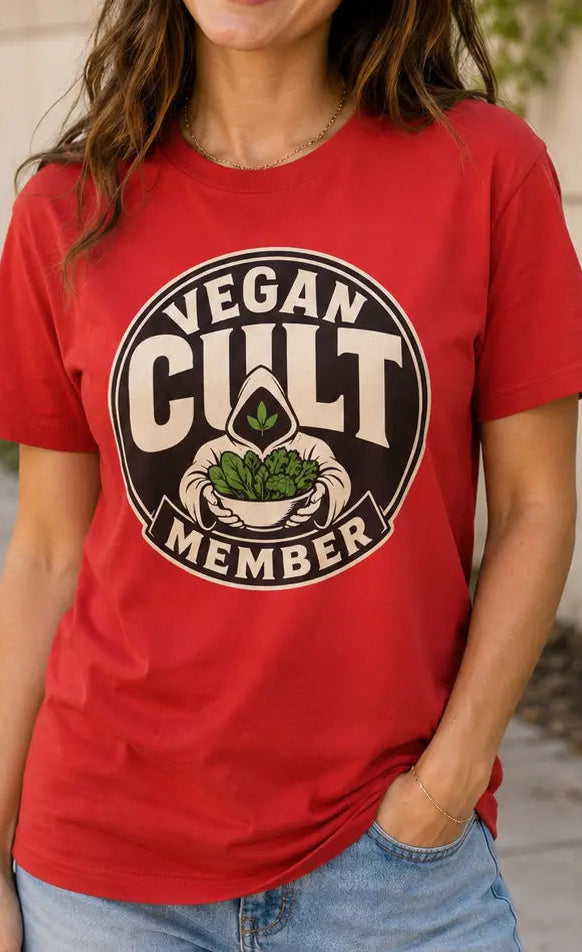 A woman wearing a red graphic t-shirt with a 'Vegan Cult Member' logo, paired with denim shorts, standing outdoors against a light-colored wall.