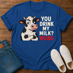 A royal blue graphic t-shirt laid flat on a wooden surface, styled with folded blue jeans and white sneakers. The t-shirt features a cartoon cow with crossed arms next to the text 'YOU DRINK MY MILK? WEIRD.