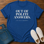 A royal blue graphic t-shirt with the text 'OUT OF POLITE ANSWERS. (TRY AGAIN TOMORROW)' in white, styled in a flat lay on a wooden background with blue jeans and white sneakers.