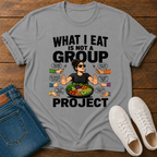gray t-shirt with a graphic of a woman eating salad and non vegan questions being thrown at her with text 'what i eat is not a group project" on a wooden board with jeans and sneakers