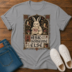 A light gray graphic t-shirt laid flat on a wooden surface, styled with folded blue jeans and white sneakers. The t-shirt features a vintage-style illustration of a rabbit holding a sign that says 'NO' surrounded by birds, mushrooms, and the text 'ASK someone ELSE'.