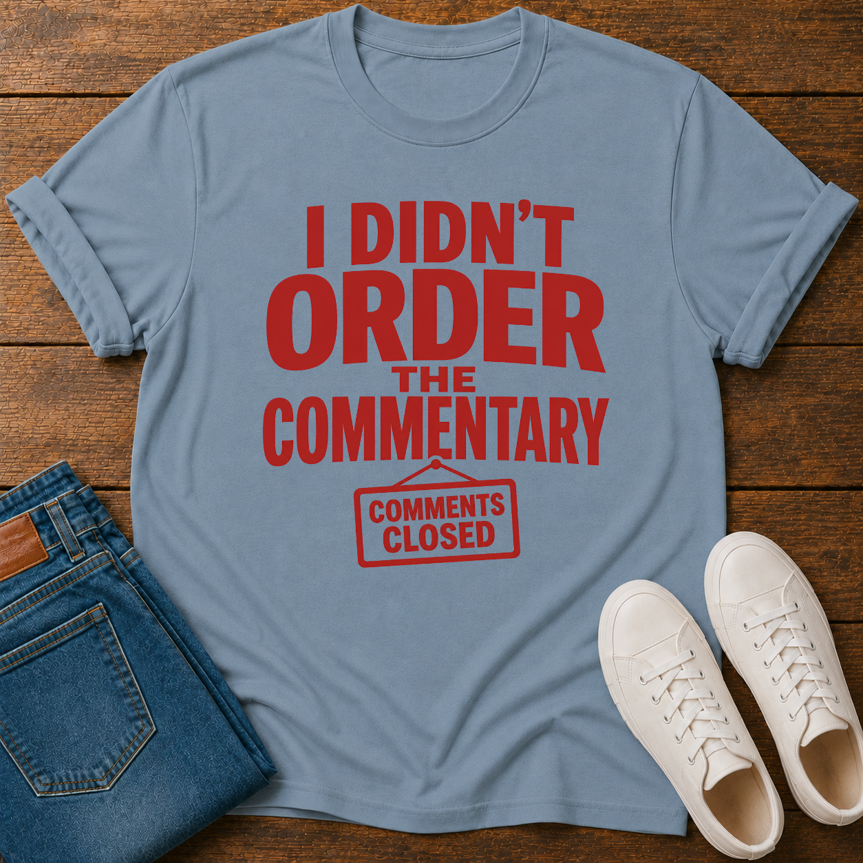 Blue t-shirt with red text 'I Didn't Order the Commentary' on a wooden surface with jeans and shoes.