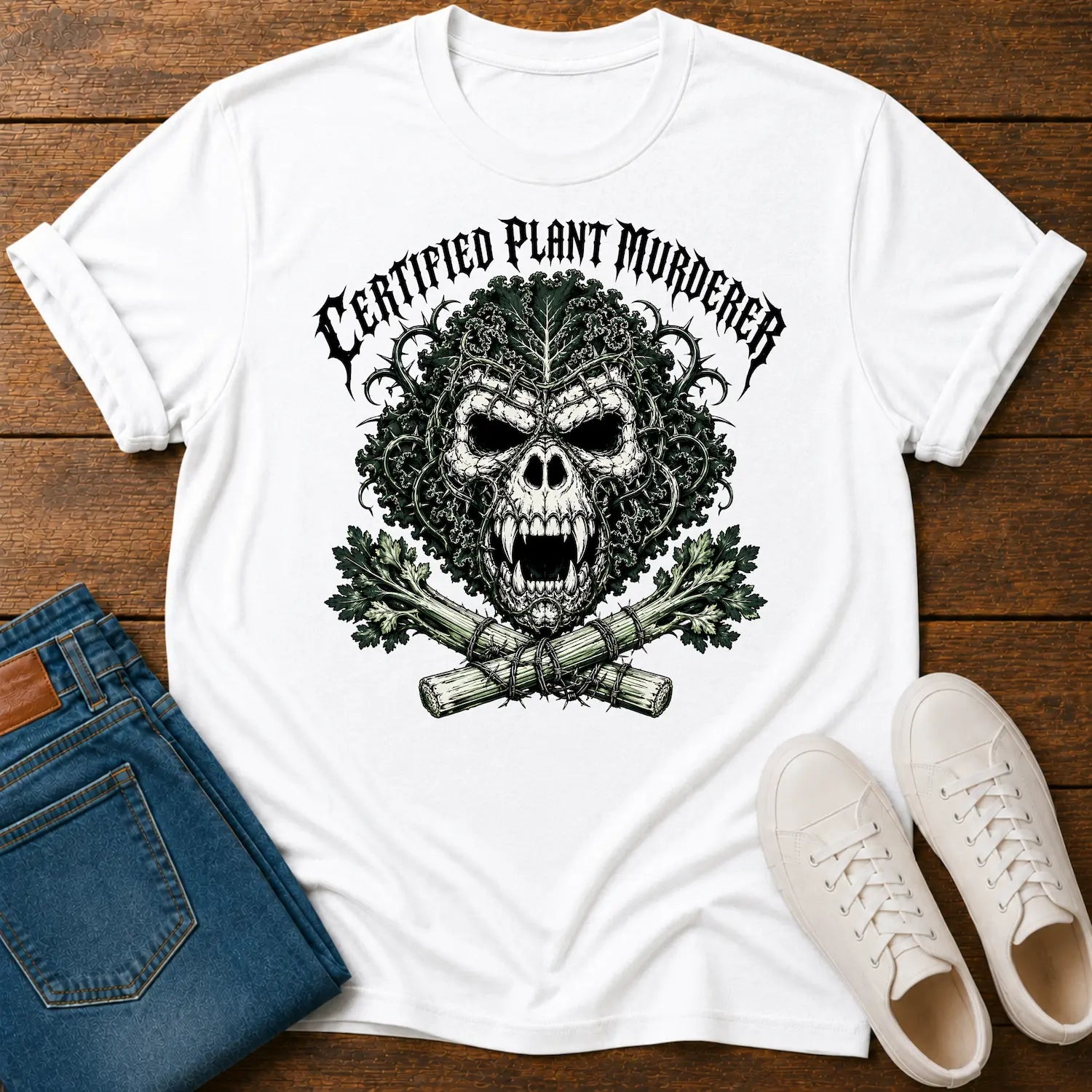 A white graphic t-shirt featuring a cartoon gorilla wearing sunglasses and holding a banana, surrounded by the text 'PROTEIN DEFICIENCY SURVIVOR' in brown and teal. The shirt is styled in a flat-lay arrangement on a dark wood background, accompanied by blue jeans and white sneakers.