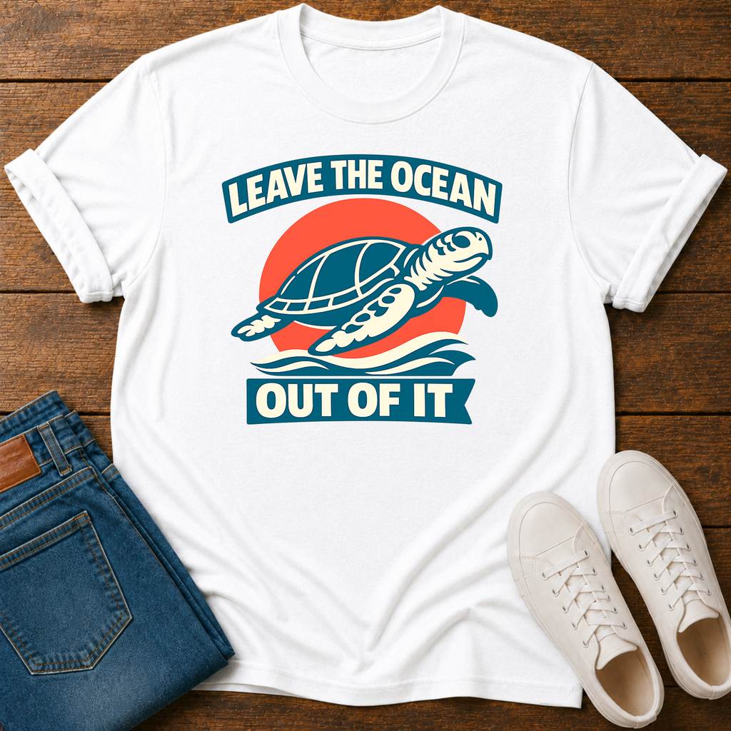 A white short-sleeve graphic T-shirt laid flat on a wooden surface, styled with folded blue jeans and white sneakers. The shirt features a retro-style turtle graphic with the text 'LEAVE THE OCEAN OUT OF IT' in blue and orange.