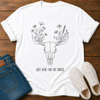 White t-shirt with image of a skull and flowers with text 'just here for the grass'